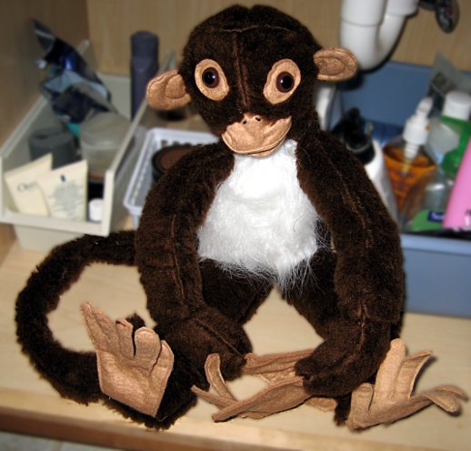 A stuffed monkey beneath a sink.